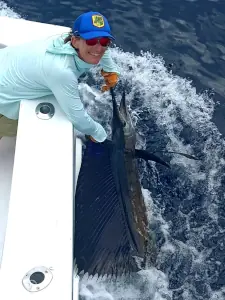 Angler in a blue hat holding a sailfish alongside the boat in Costa Rica