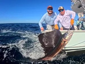Two fishermen smiling with a sailfish alongside the boat in Guatemala