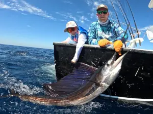 Two generations of anglers holding a sailfish alongside the boat in Guatemala