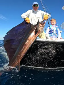 Younger and older anglers holding a sailfish alongside the boat in Guatemala