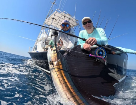 Fish the World owner Thomas Hunt holding a Sailfish along side an offshore fishing boat.